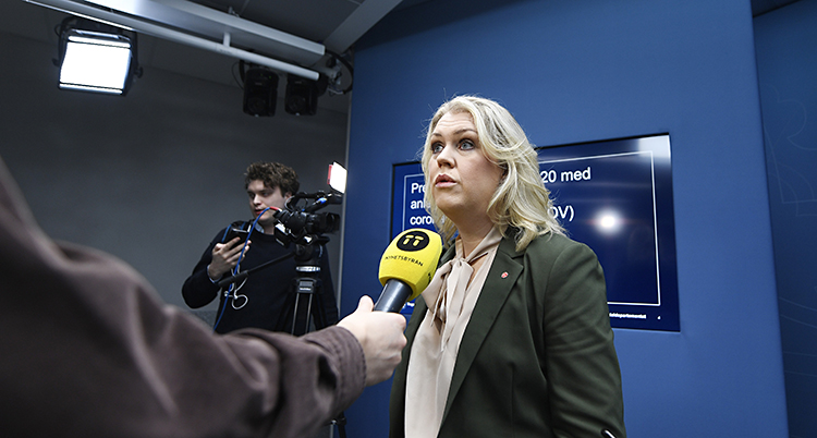 Lena Hallengren i ett blått rum. En mikrofon sträcks fram mot henne.