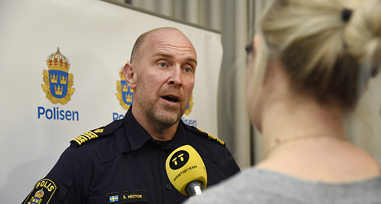 Han har polisuniform och blir intervjuad av en journalist med mikrofon