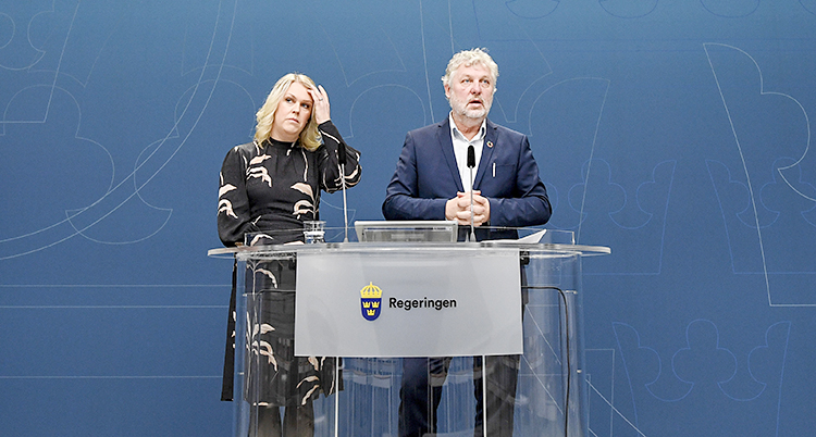 De står vid en blå vägg och pratar i mikrofon