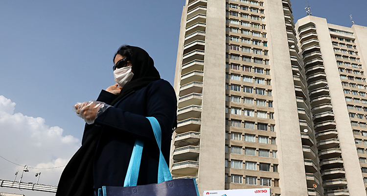 En kvinna i Iran har mask i ansiktet. Bakom henne finns ett högt hus.