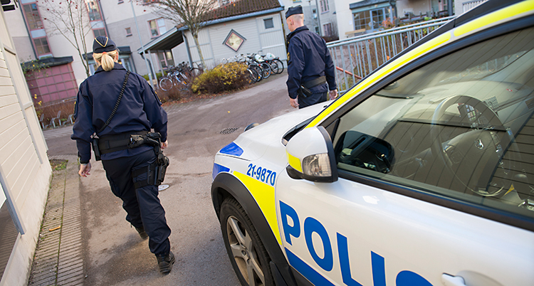 Två poliser går framför en parkerad polisbil. De är på väg mot ett bostadsområde.