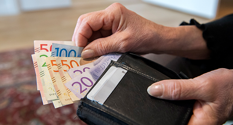 Bilden visar en person som tar ut sedlar ur en plånbok. Vi ser bara plånboken och händerna.
