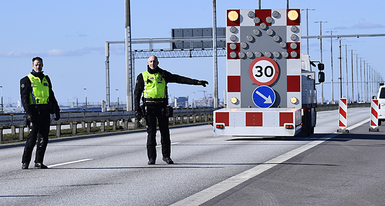 Två poliser i gula västar. Pekar åt en bil att svänga åt sidan