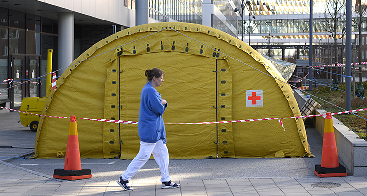 En kvinna i sjukvårdskläder går utanför ett stort gult tält