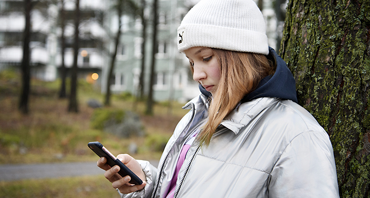 Bilden visar en tjej som håller i en telefon. Hon är utomhus.