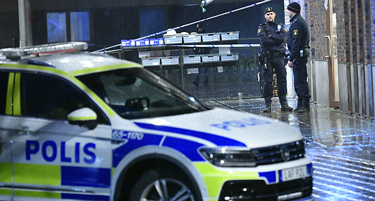 En polisbil framför en avspärrning där det står två poliser.