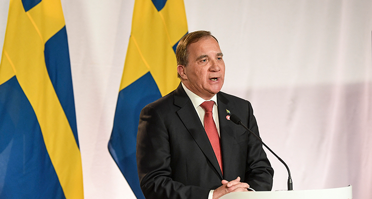 Han står framför svenska flaggor och talar i mikrofon
