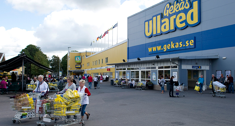 Gekås fasad. Folk lämnar butiken med varuvagnar fyllda med fulla plastpåsar.