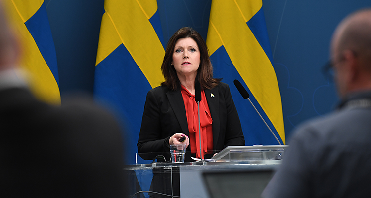 Hon pratar på en träff med journalister. I bakgrunden syns svenska flaggor.