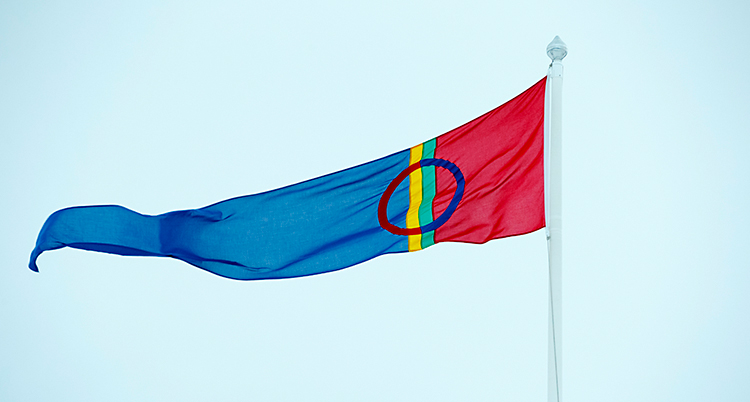 Den samiska flaggan vajar i vinden. Den hänger på en flaggstång. Den är röd, blå, grön och gul.
