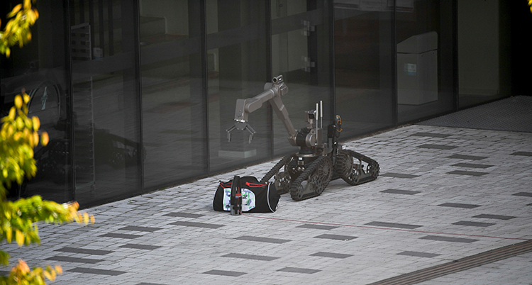 En robot är utanför ett hus. Den är nära en väska.
