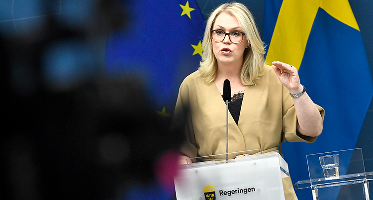 Hon har ljust hår, glasögon och pratar i mikrofon