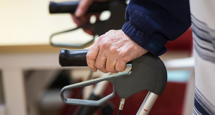 En äldre med en rollator. Vi ser händerna på handtagen.