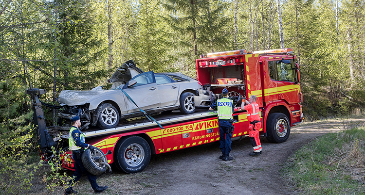 En bärgningsbil med en kvaddad bil på flaket. Två poliser står bredvid.