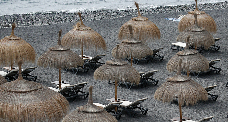 En strand med parasoller i bast och tomma solstolar