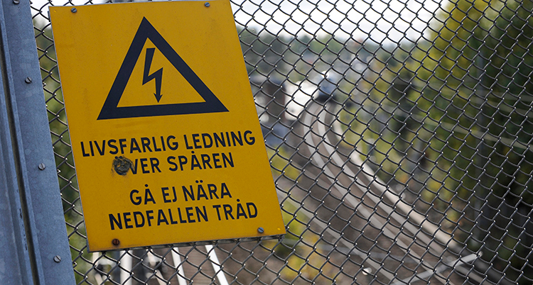 en bild på ett spår och en skylt som varnar för spänning i ledningar.