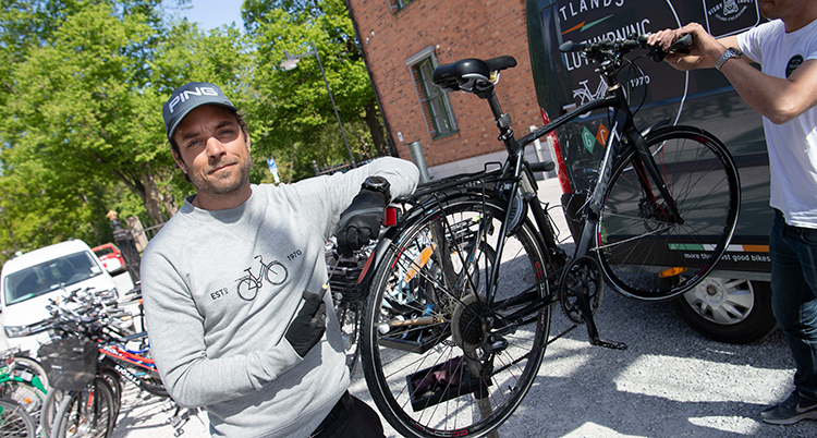 En man vid en cykel som står på en ställning. Han håller på att laga den.