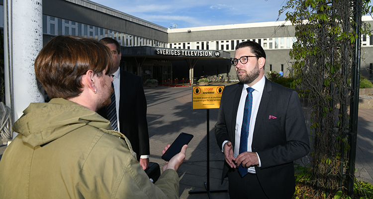 Jimmmie Åkesson framför SVTs entré blir intervjuad av en journalist med mikrofon.