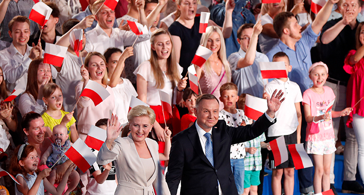 En massa människor med polska flaggor. Framför den stor presidenten och hans fru och vinkar.