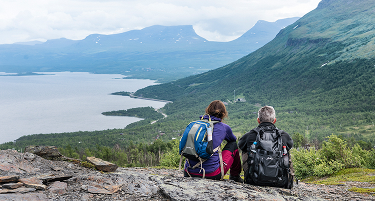 Två personer sitter ner på ett fjäll och tittar på en utsikt.