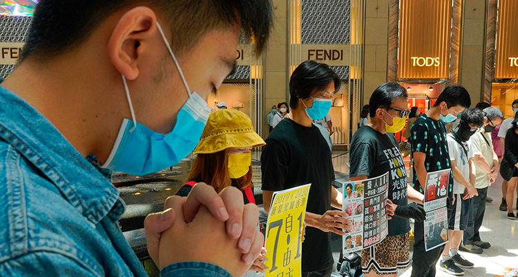 Människor i Hongkong protesterar mot Kinas nya lag. De har på sig munskydd och håller i skyltar.