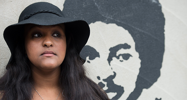 Betlehem Isaak har en svart hatt på sig. Hon står vid en vägg. På väggen är det en bild på hennes pappa, Dawit Isaak.