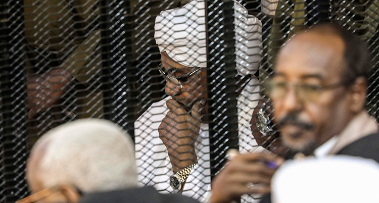 Omar al-Bashir med handen lutad mot huvudet bakom ett galler.