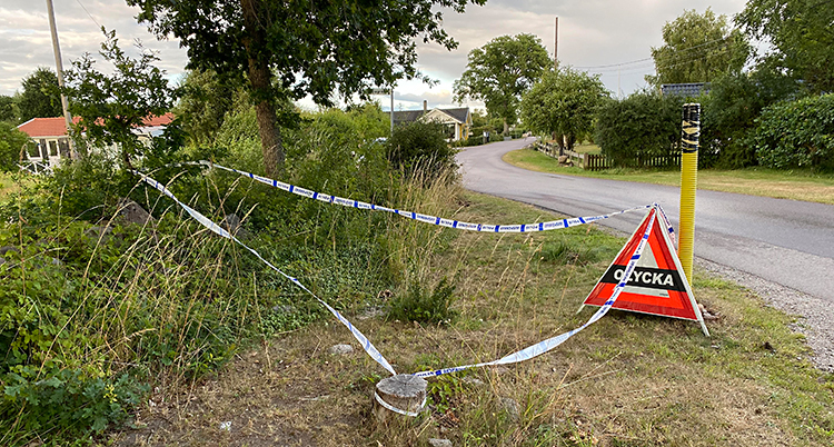 Bilden visar en väg. Bredvid vägen finns det en triangel där det står Olycka. Poliserna har satt upp blå och vita band.