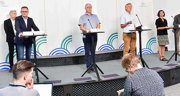 Flera personer står på en scen. De har varsitt litet bord. På varje bord finns en mikrofon.