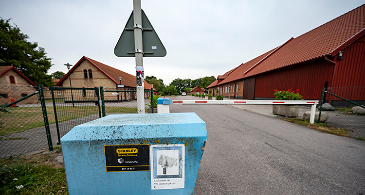 Vi ser en väg som leder fram mot några hus. Innan husen finns det en vägspärr.