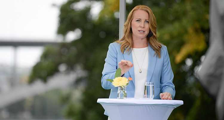 Annie Lööf står i en talarstol utomhus. Hon har blå kavaj. Framför henne står en blomma och ett glas vatten.