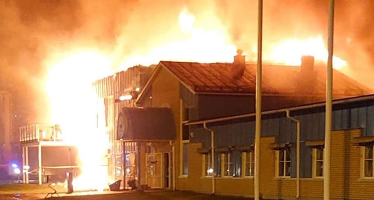 Massor av lågor sprutar ut ur huset. Det är kväll och mörkt på bilden.