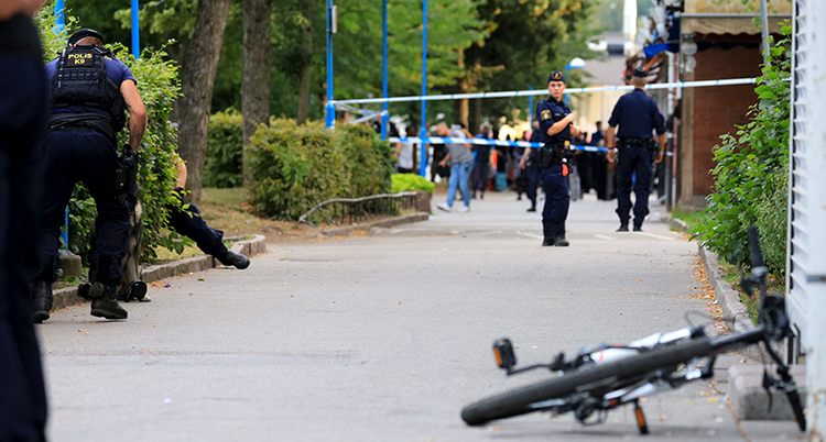Poliser som står på en gångväg där det skett en skjutning. En cykel ligger på gångvägen.