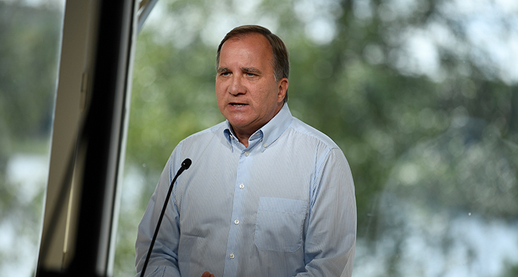 Löfven ser allvarlig ut och talar. Ett träd syns bakom honom. Han har skjorta utan slips.