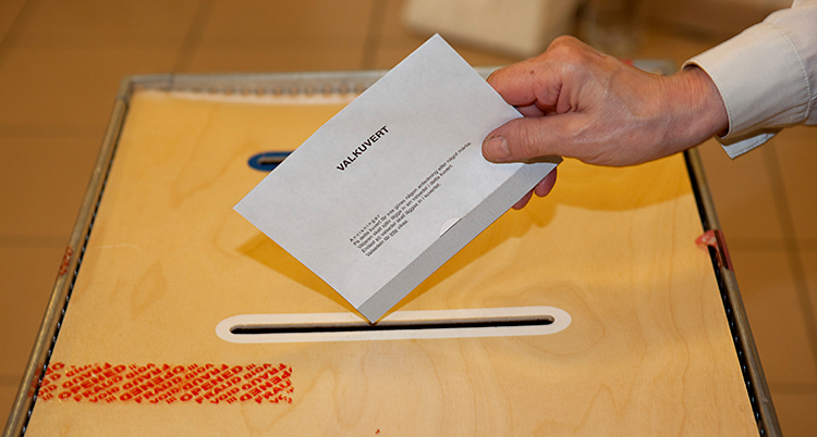 Vi ser en hand som lägger ner ett valkuvert i en valurna.