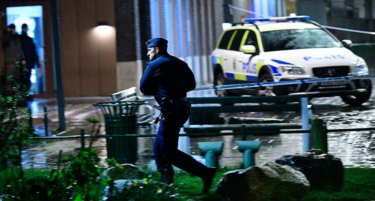 en polis springer framför en polisbil.