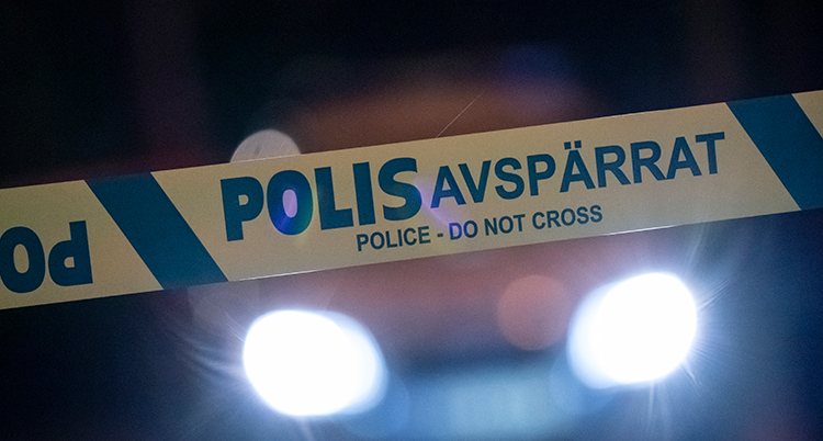 ett plastband från polisen i fokus. Bakom lyser två billyktor.