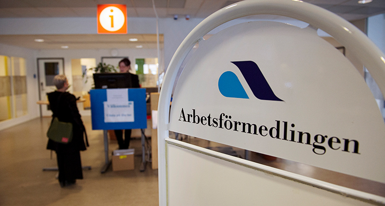 En kvinna i bakgrunden av bilden står framme vid arbetsförmedlingens kassa. I förgrunden Arbetsförmedlingens skylt.