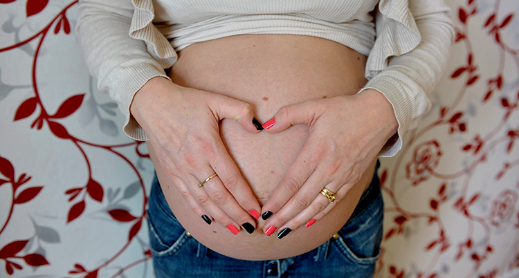 En gravid kvinna har dragit upp tröjan så att magen syns. Hon håller händerna på magen. Kvinnans ansikte syns inte.