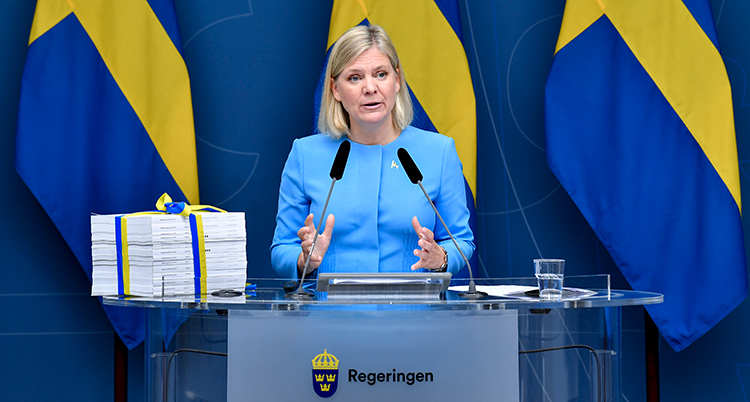 Andersson står i en talarstol. Bakom henne är svenska flaggor. Bredvid henne ligger alla förslag i en tjock biunt. Ett blågult snöre är knuten runt bunten.