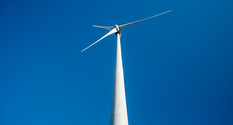 En pelare till ett vindkraftverk fotat underifrån. Högst upp är själva snurran. Bakgrunden är en djupblå himmel.