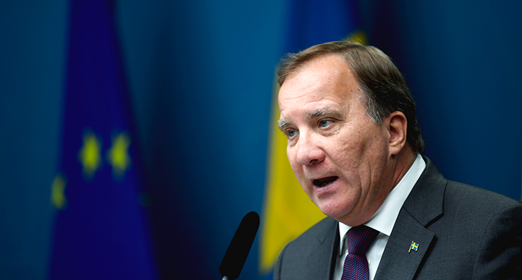 Löfven ser allvarlig ut. Han talar i en mikrofon. Bakom honom är den svenska flaggan, men den syns dåligt för att den är så nära.