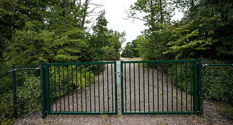 Ett staket spärrar av en väg. Staketet är ungefär en meter högt. Bredvid vägen finns skog.