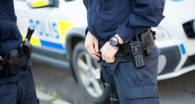 Två poliser står och pratar. Deras huvuden syns inte på bilden. De står framför en polisbil.