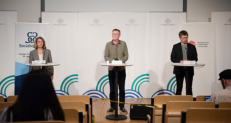Tre personer står på en scen. De pratar i varsin mikrofon. Längst till vänster står en kvinna. De andra två är män.