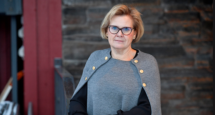 Hon tittar in i kameran. on har kort blont hår och glasögon.