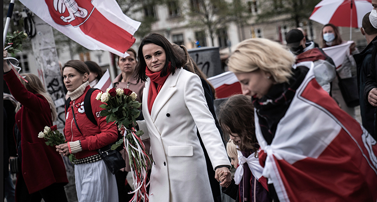 Hon går i en demonstration. Hon har flera andra människor runt sig. Hon har vit kappa och kort brunt hår.
