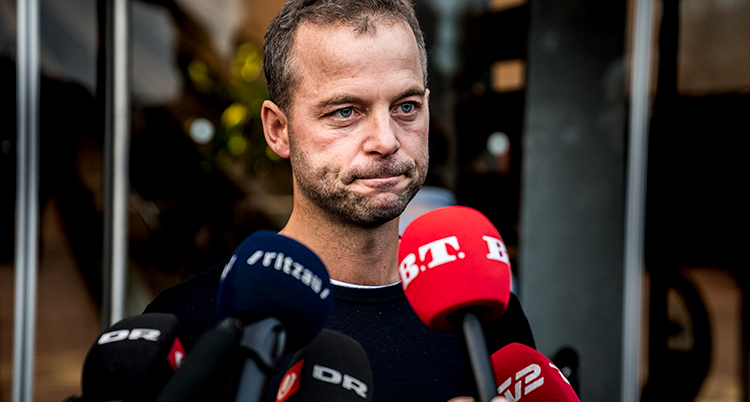 Politikern ser sammanbiten ut framför reportrar som sträcker fram sina mikrofoner.