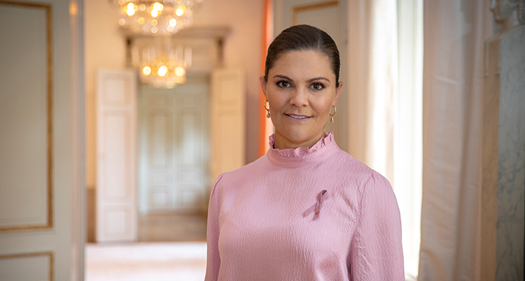 Hon har en rosa blus på sig. På bröstet sitter det Rosa bandet fast.