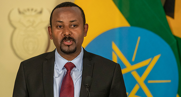 Abiy Ahmed står på en scen och pratar. Han har har kort och ett litet skägg runt munnen. Han har kostym och en röd slips.